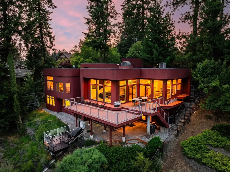Twilight aerial view of the remodeled Hayden Lake home with a multi-level deck and forested lot