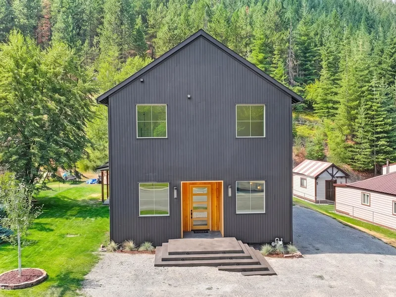 Black board-and-batten custom home with a cedar entry against a forested Silver Valley hillside